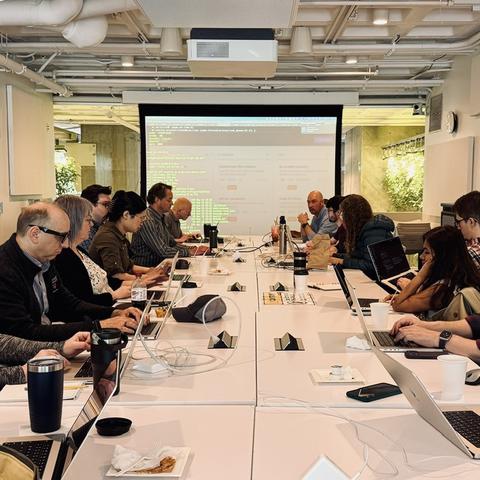 Staff on their laptops sit across from each other at a table during the LTS Hackathon.